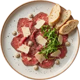 Rundercarpaccio van boven met parmezaanschilfers, rucola, truffelmayonaise en stokbrood op een wit bord