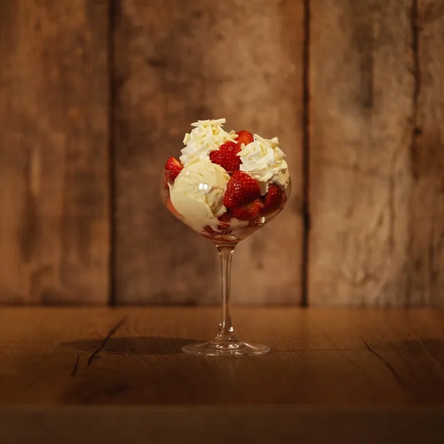 Coupe Romanoff op de houten toog: vanille-ijs met verse aardbeien en room in een glazen coupe