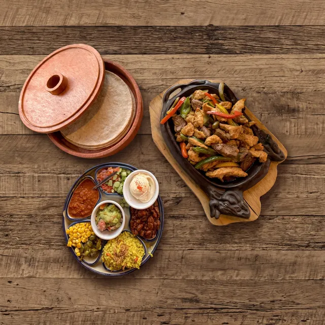 Fajitas Beef van boven: reepjes ossenhaas met paprika en ajuin in de gietijzeren pan, met tortilla's en schaaltjes garnituur