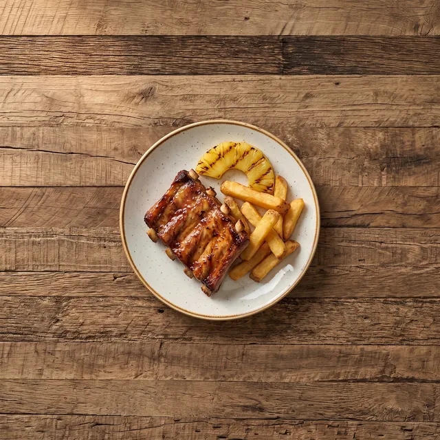 Kinderportie spareribs van boven met frietjes en gegrilde ananas op een klein bord