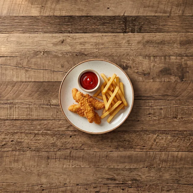Gepaneerde kippenreepjes met frietjes en ketchup van boven op een klein bord