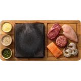 Stonegrill van boven: hete steen op een plank met rauwe steak, kip, hamburger, zalm en scampi en drie sausjes
