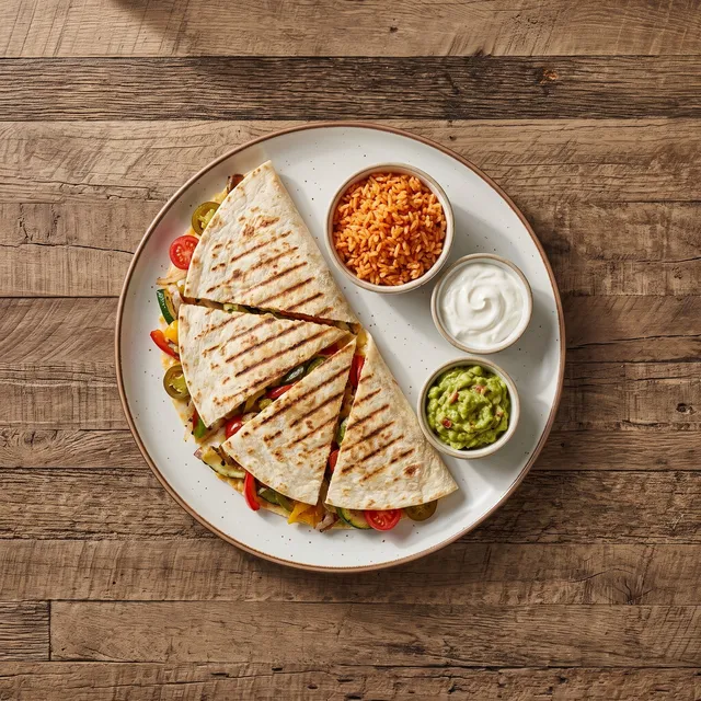 Quesadilla grande veggie van boven: gegrilde tortilla in punten met groenten en kaas, met Mexicaanse rijst, zure room en guacamole in aparte potjes