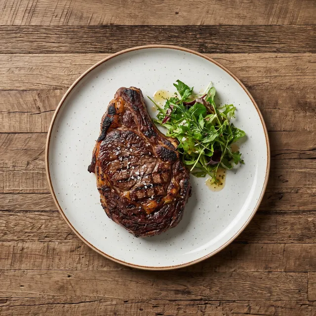 Ribeye uit de Josper van boven, met een korst van het houtskoolvuur en een fris slaatje op een wit bord