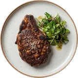 Ribeye uit de Josper van boven, met een korst van het houtskoolvuur en een fris slaatje op een wit bord
