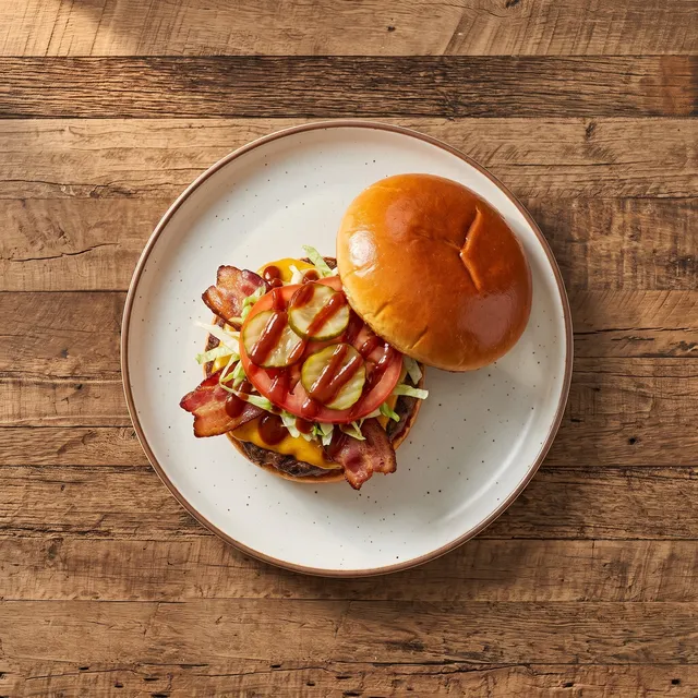 Smokey burger van boven met cheddar, gerookte bacon, sla, tomaat en augurk, het bovenste broodje ernaast