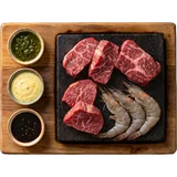 Stonegrill surf en turf van boven: hete steen met rauwe steak en scampi en drie sausjes op een plank