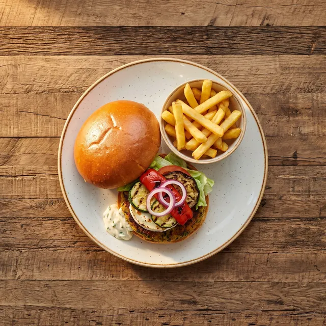 Veggie burger van boven met gegrilde groenten, tomaat en rode ajuin, met frietjes in een schaaltje
