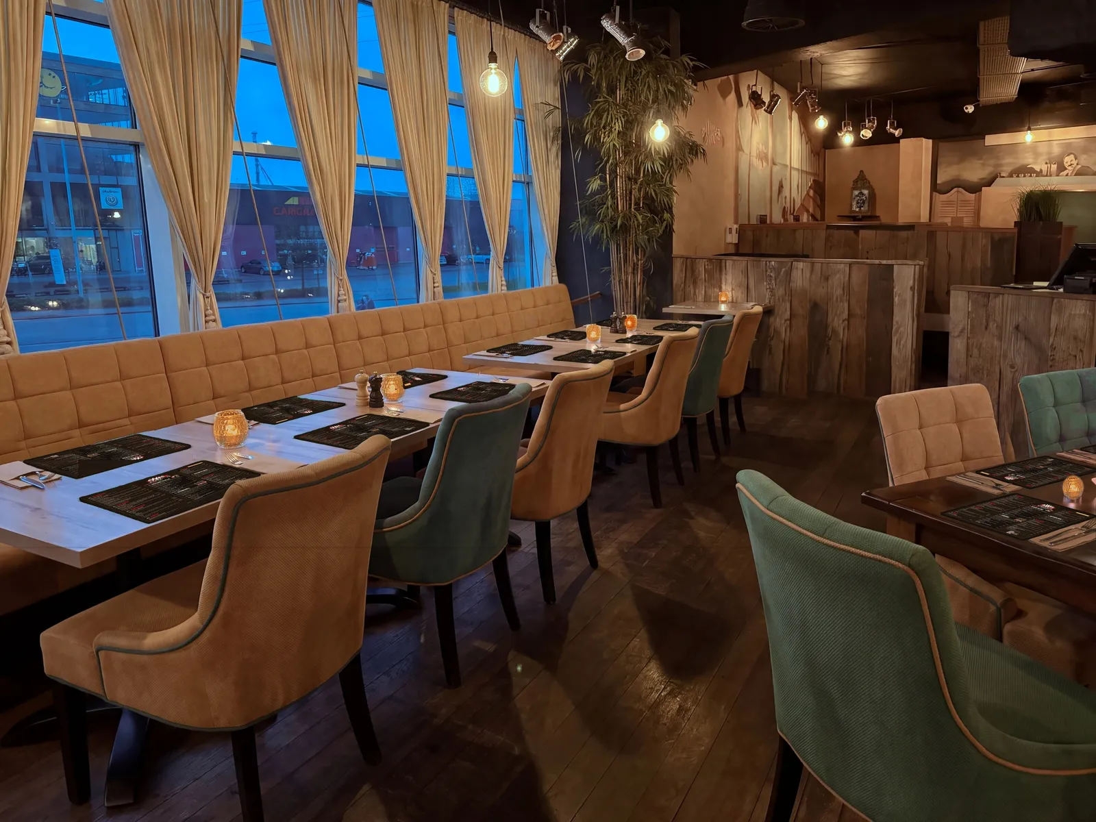 Lange gedekte tafels voor groepen Lange rij tafels langs de oker bank en de ramen van AXXES, gedekt met menukaart-placemats en amberkleurige kaarsjes