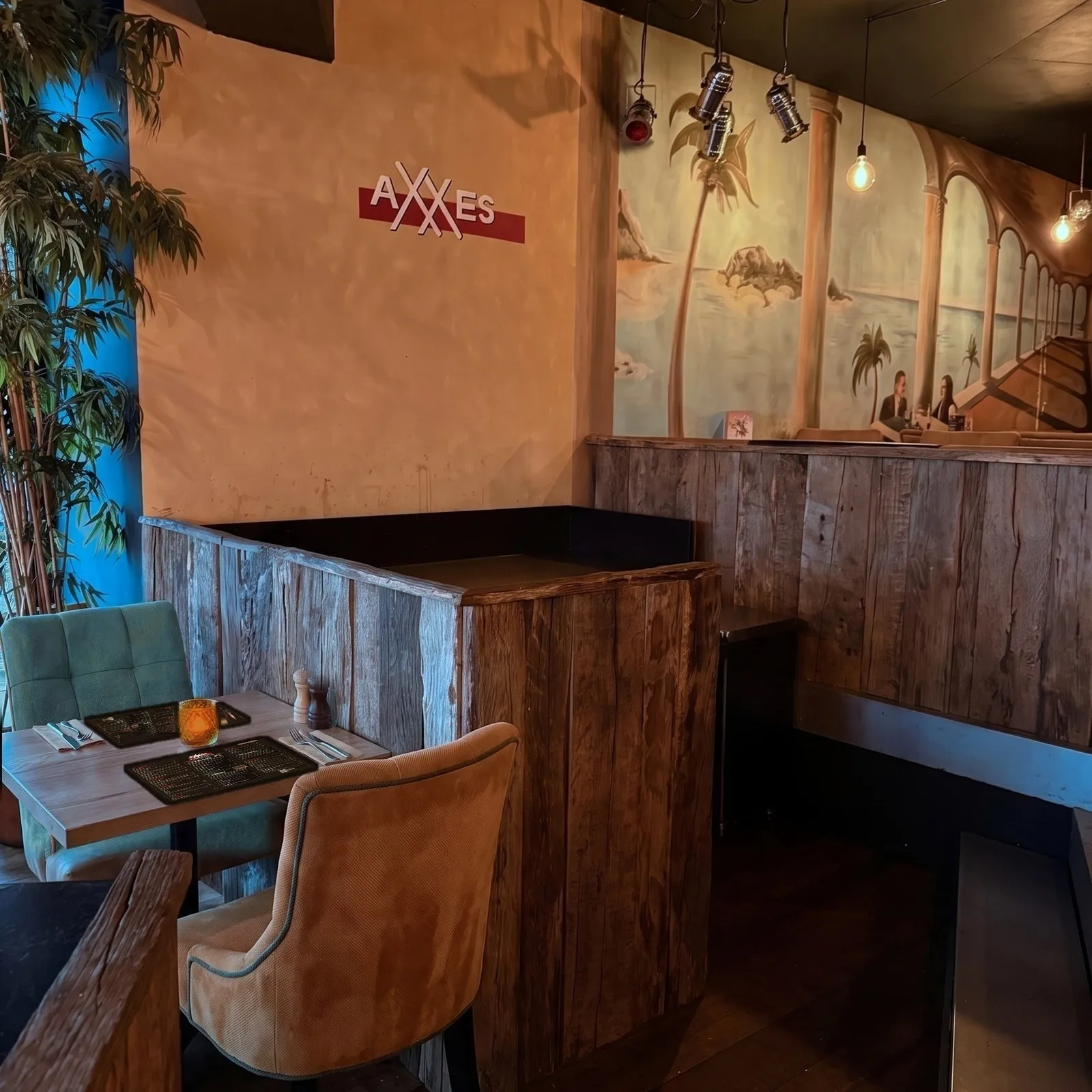 Table pour deux dans la niche d'AXXES, avec des sets de table imprimés de la carte, des serviettes beiges, une bougie ambrée et la peinture murale