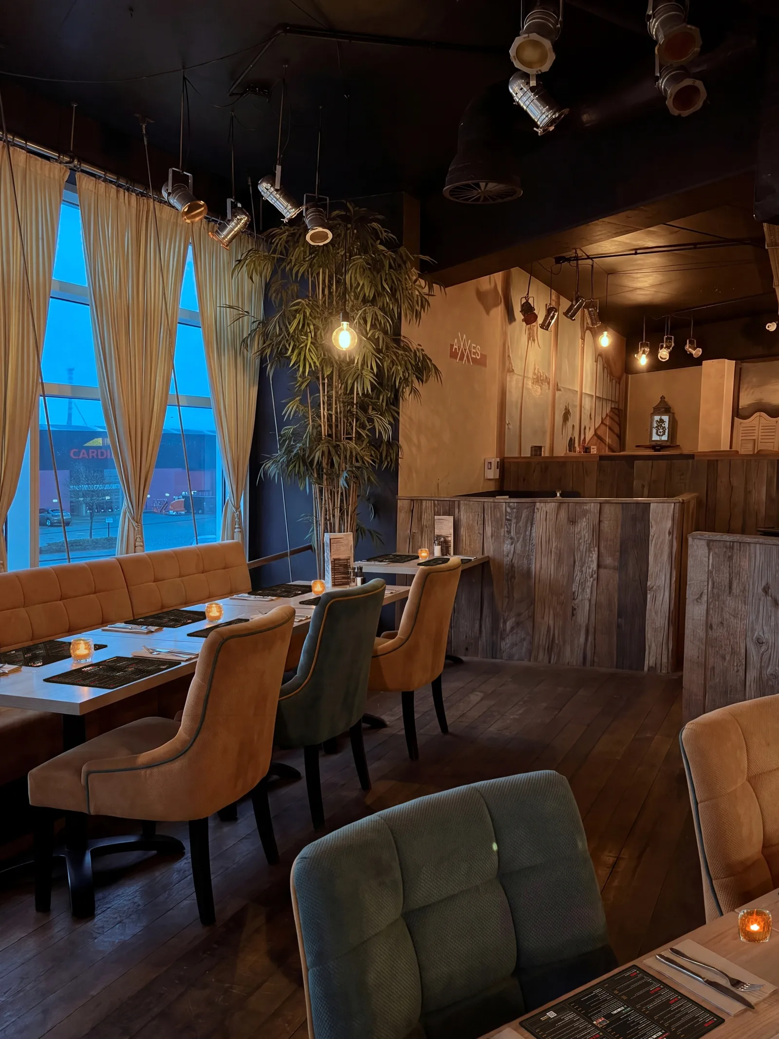 Zaal van AXXES bij avond: tafels met de menukaart als placemat, beige servetten met bestek en amberkleurige kaarsjes