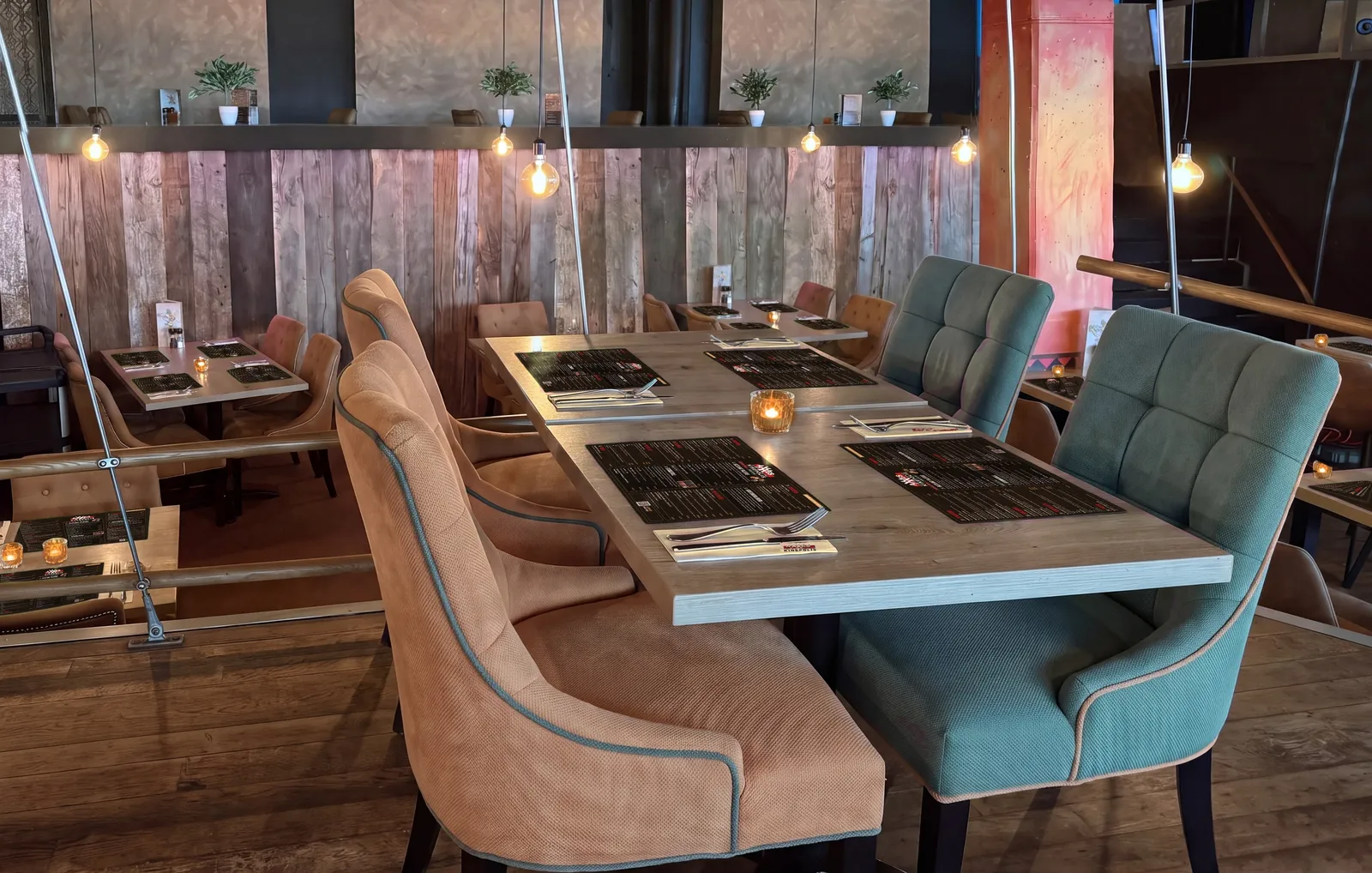 Tafels voor de barnhouten wand van AXXES, gedekt met menukaart-placemats, beige servetten met logo en amberkleurige kaarsjes